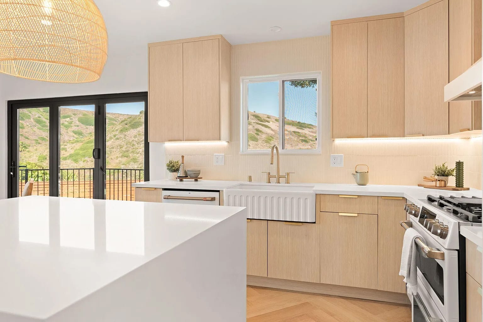Kitchen with a farmhouse sink at the window, white oak cabinets, and glass doors to a hillside view, DHRH Campanil renovation