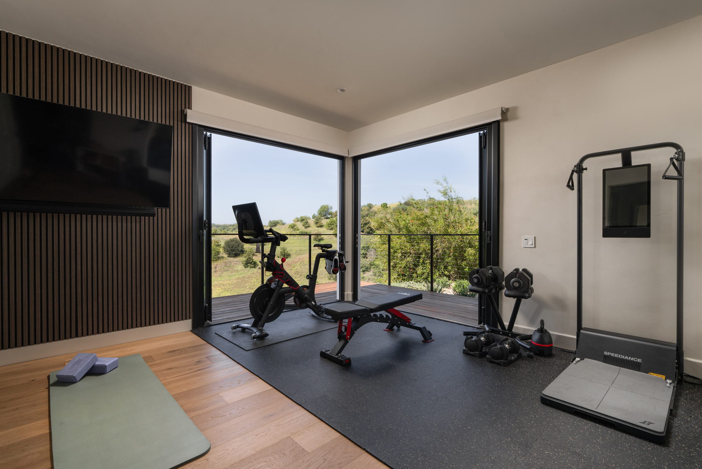 Home gym with a wood slat accent wall and corner glass doors opening to a hillside deck, DHRH Mission Canyon renovation