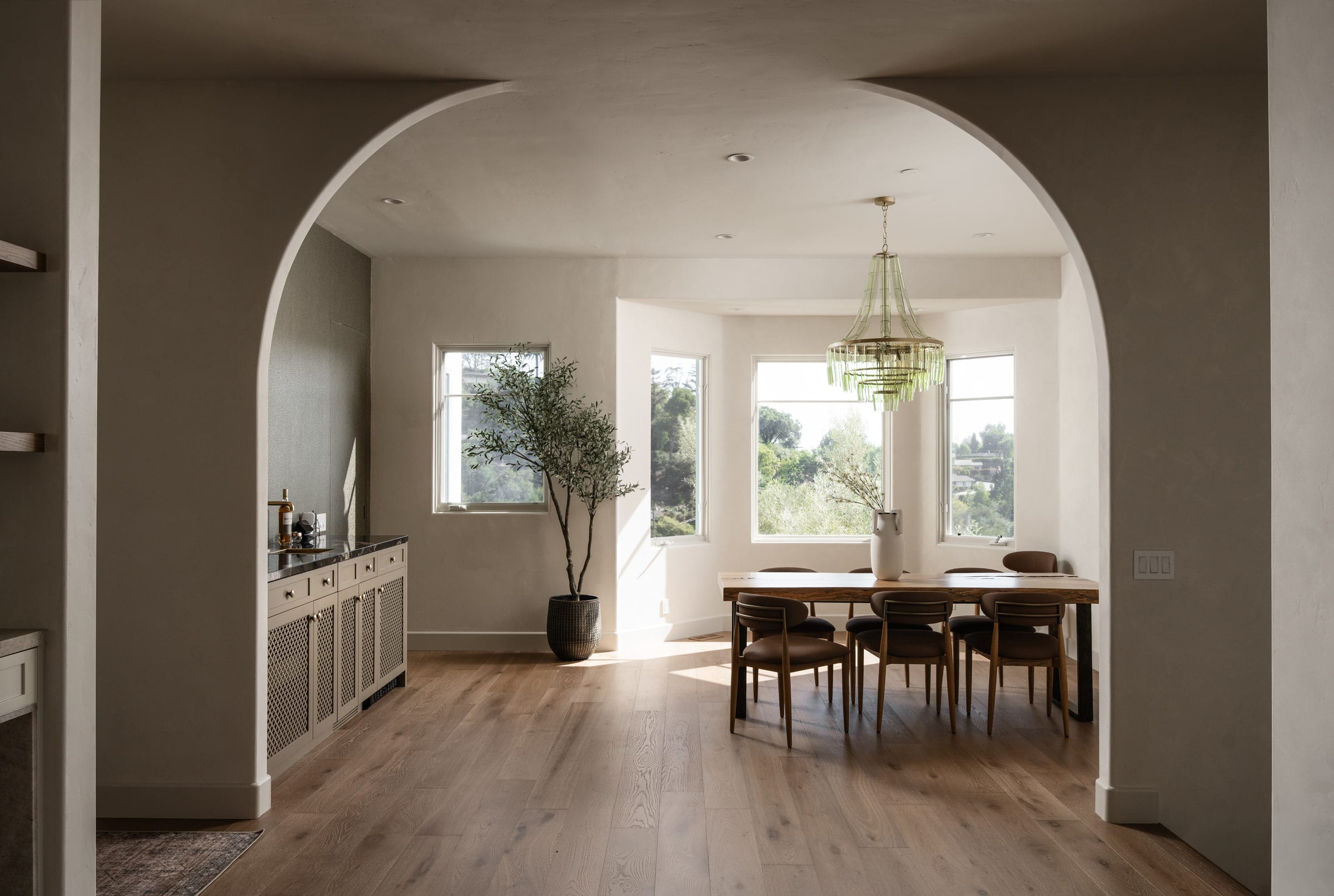 Dining room seen through an arched doorway, with a tiered glass chandelier and bay window hill views, DHRH Mission Canyon renovation