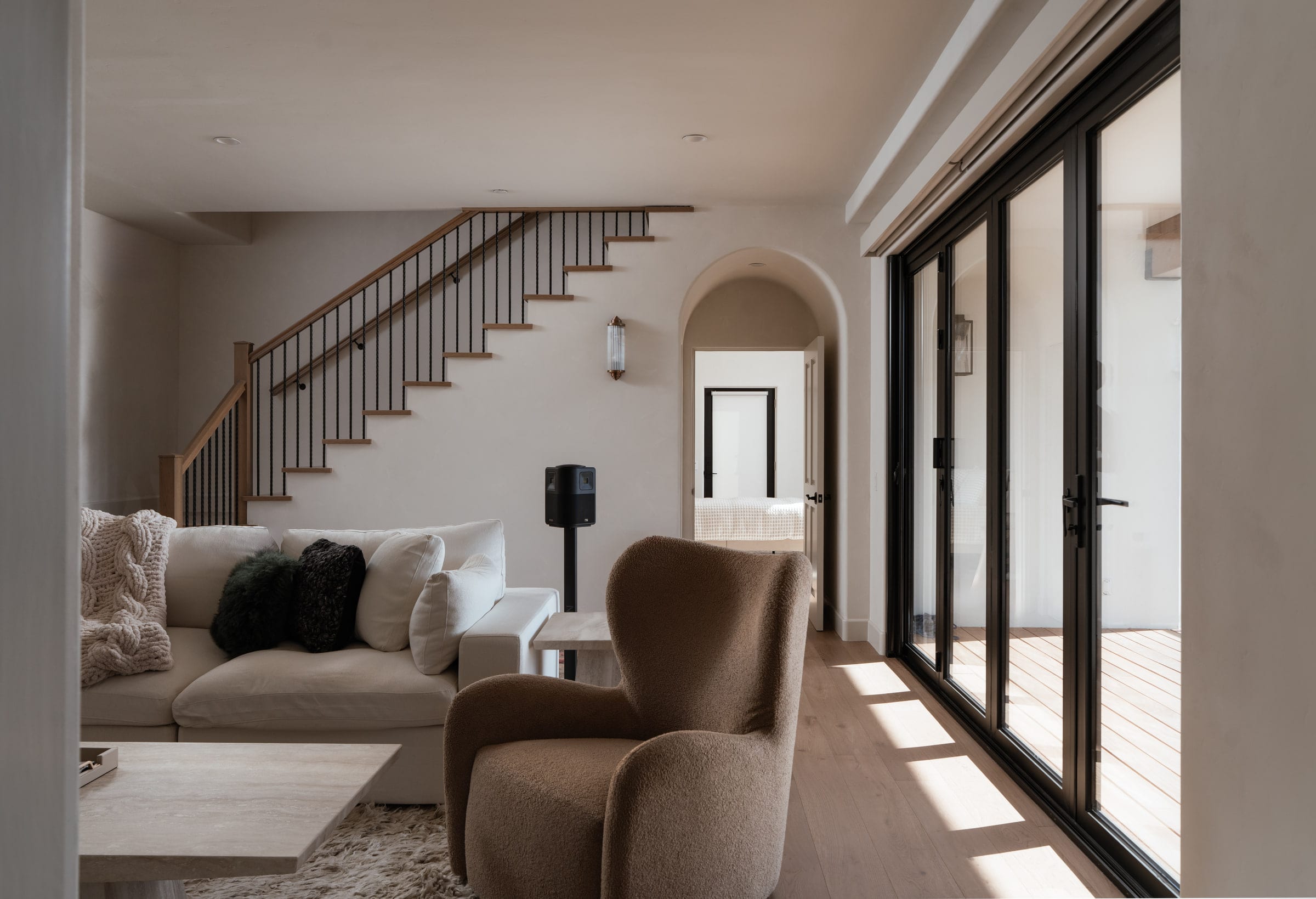 Living room with a wood and iron staircase, a cream sectional sofa, and black-framed sliding glass doors, DHRH Mission Canyon renovation