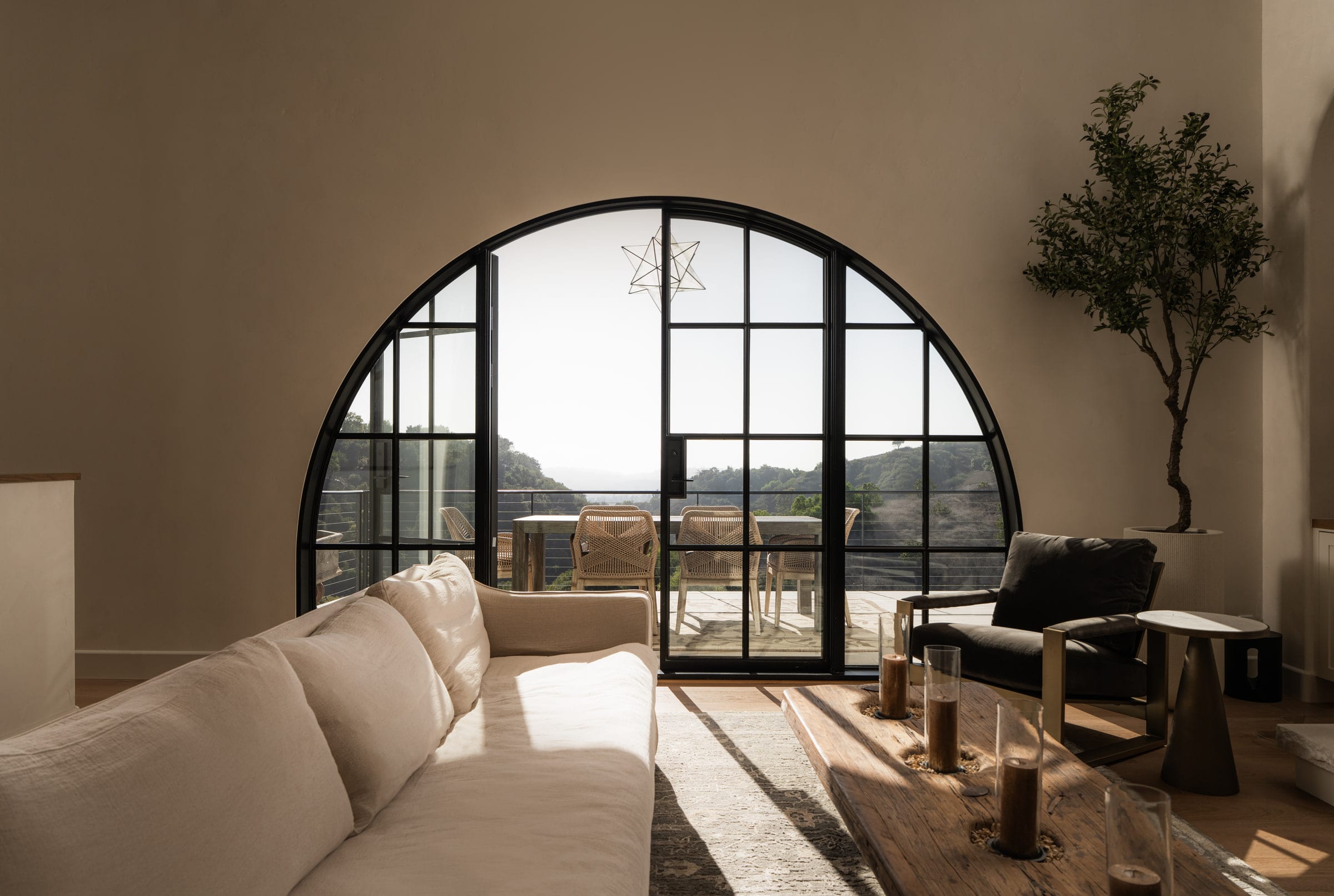 Living room with a large arched steel-framed window wall opening to a deck with hillside views, DHRH Mission Canyon renovation