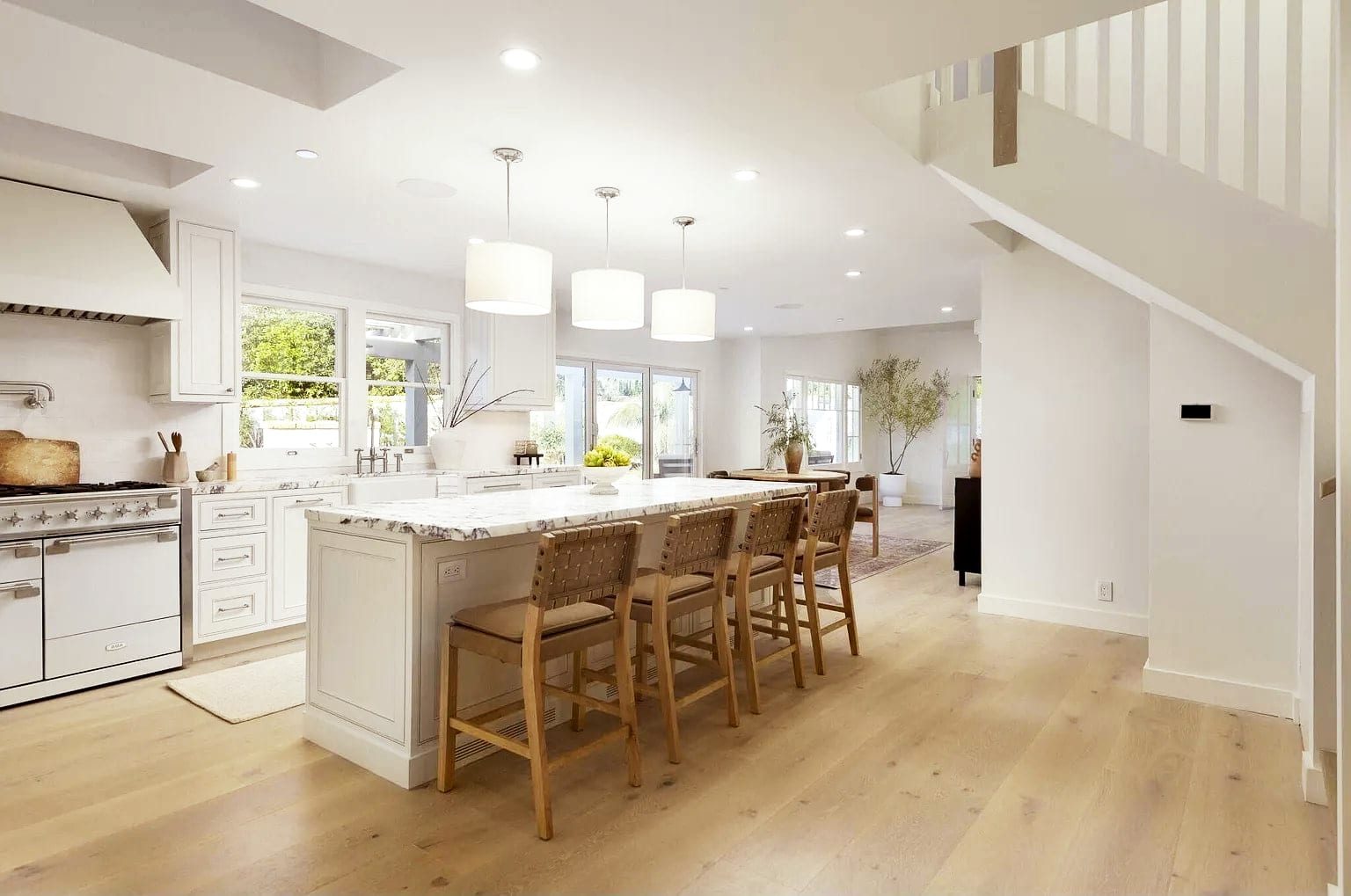 Open kitchen with a veined marble island, woven leather bar stools, and white oak floors, DHRH Montecito renovation