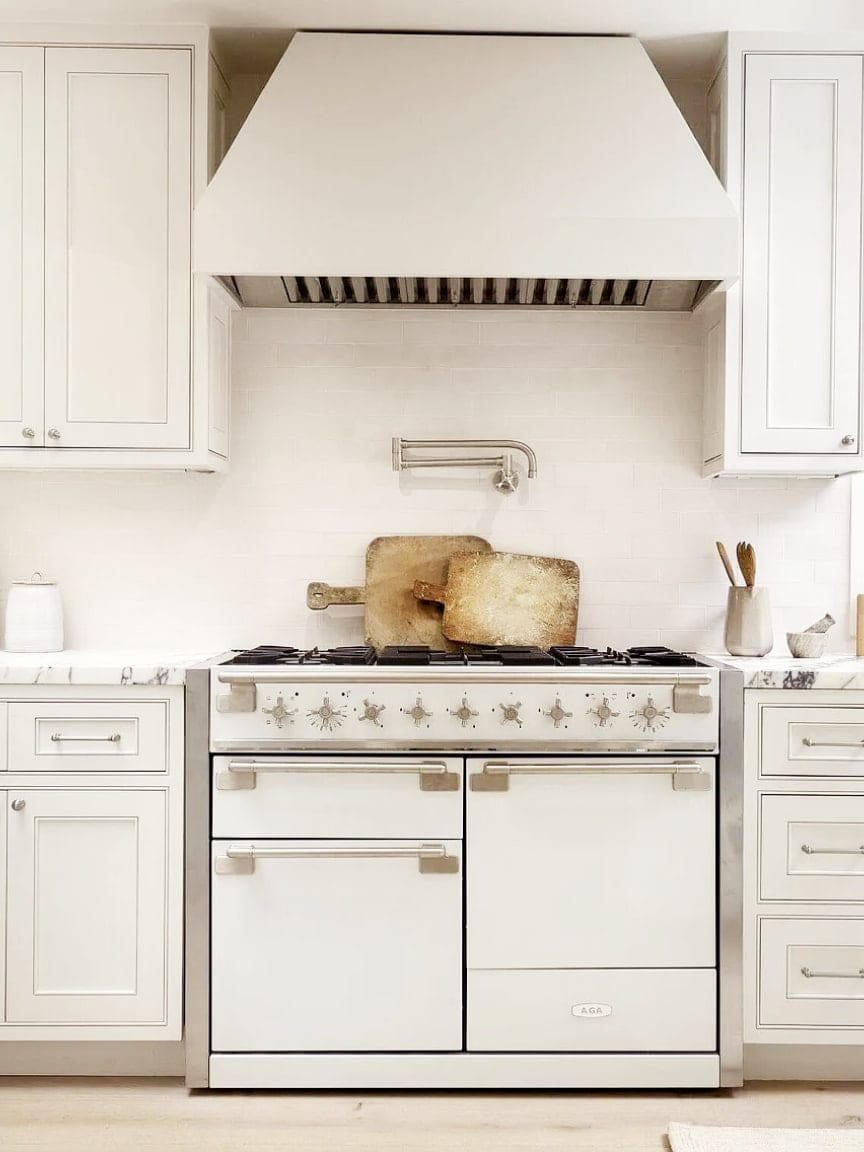 A white AGA range under a plaster hood with a pot filler and marble counters, DHRH Montecito renovation