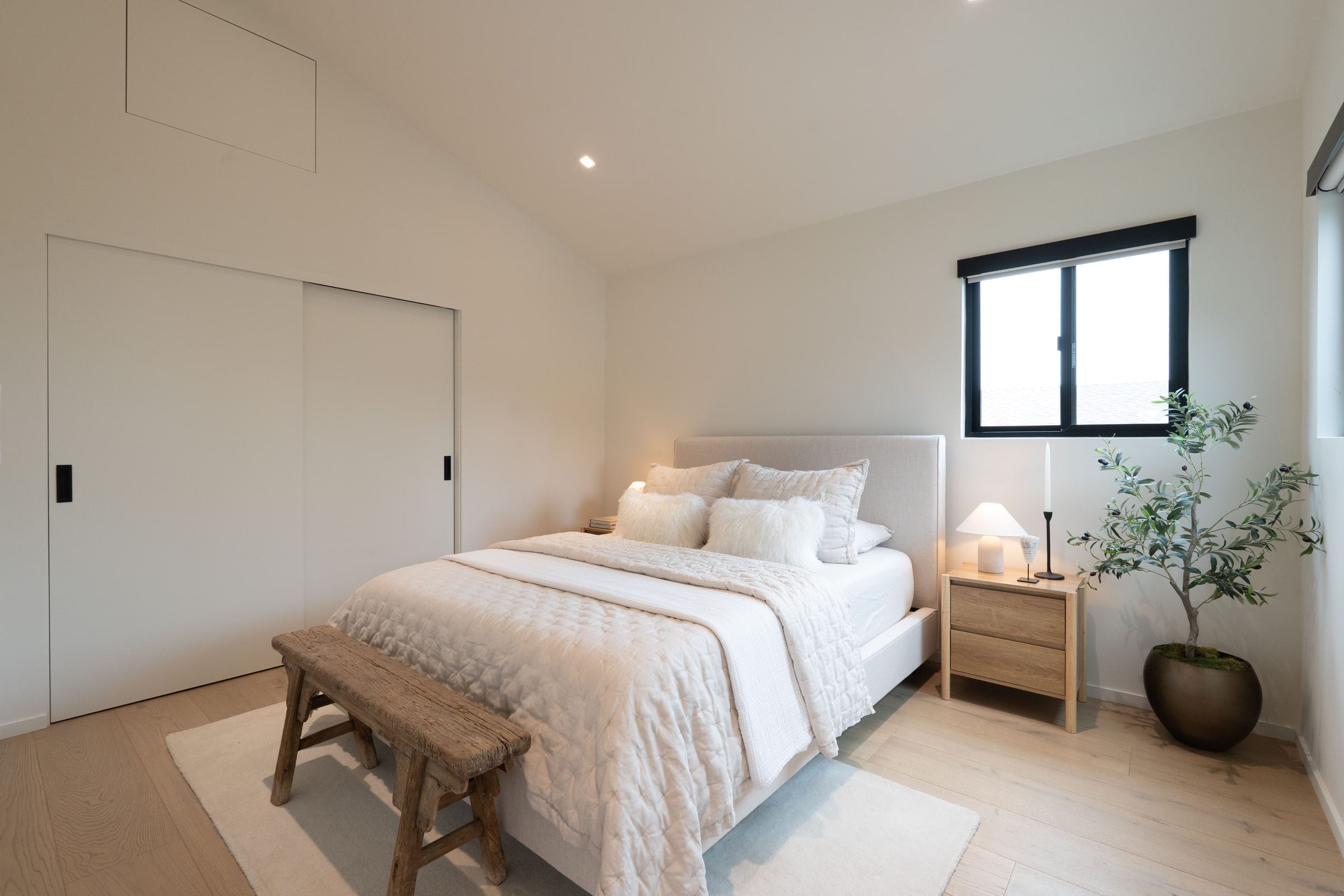Guest bedroom with a linen upholstered headboard, faux-fur pillows, wood nightstand, and a potted olive tree, DHRH Padaro Lane renovation