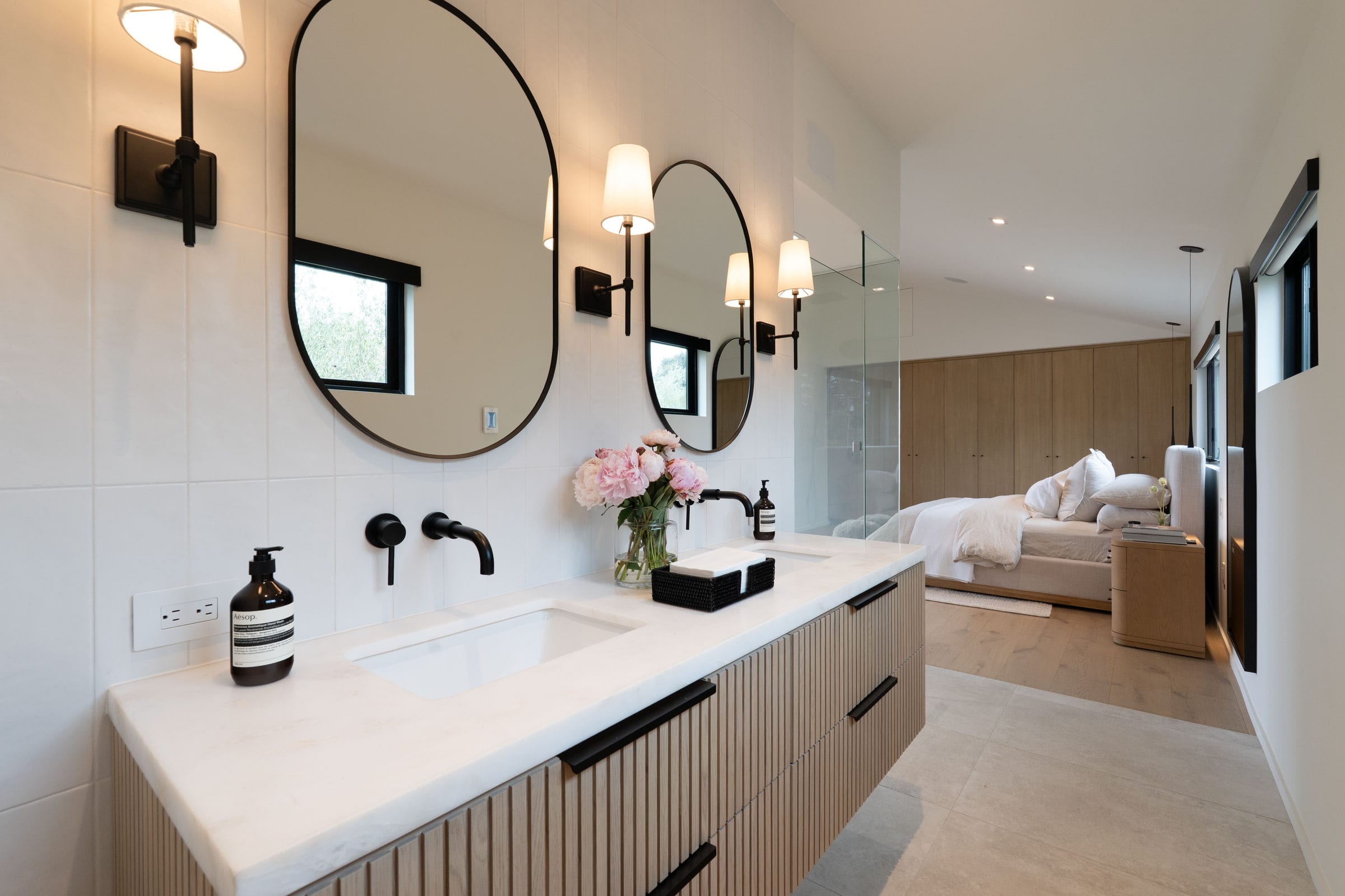 Primary bath double vanity with black oval mirrors, wall-mounted faucets, and a view into the bedroom beyond, DHRH Padaro Lane renovation