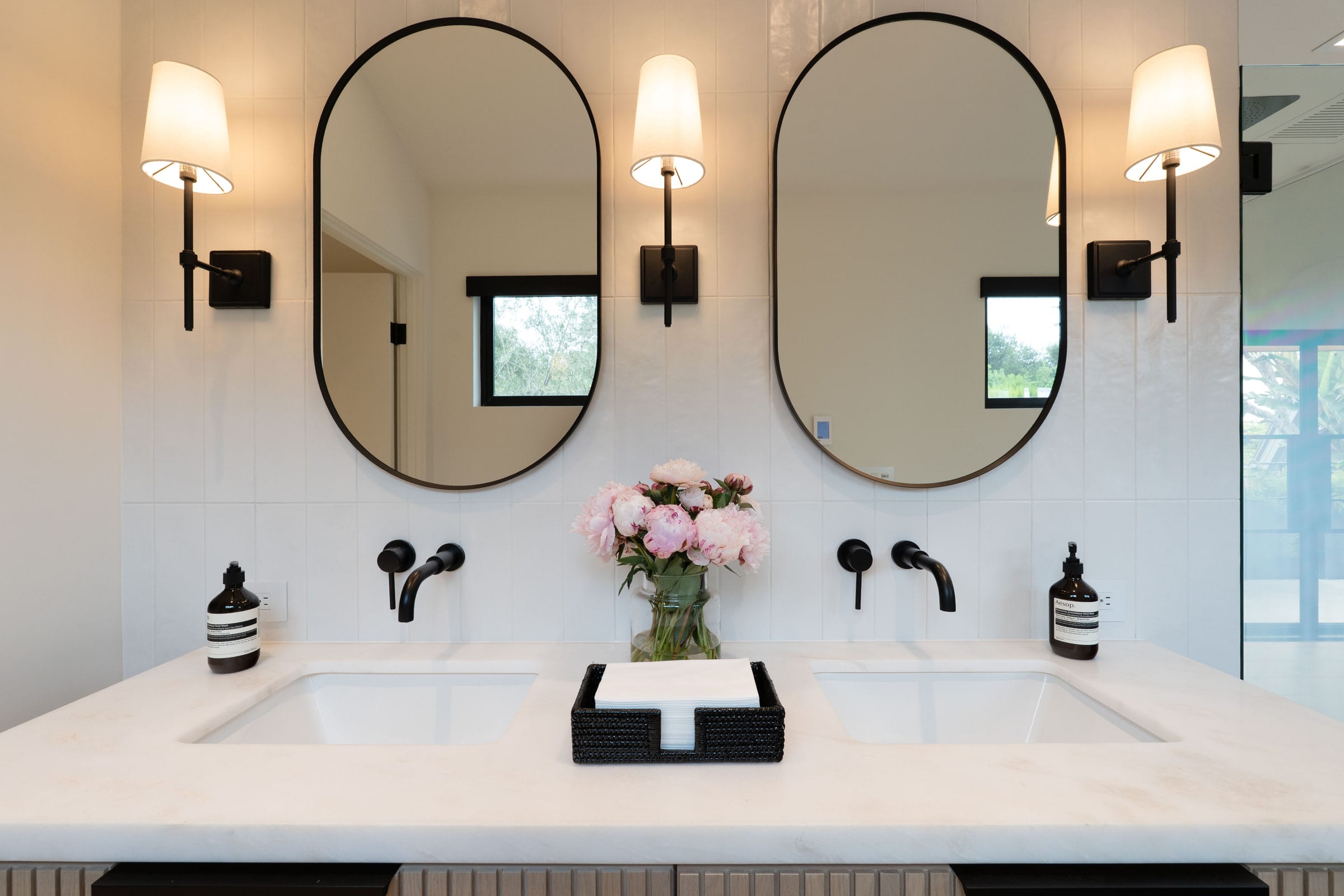 Close-up of the primary double vanity with dual undermount sinks, black sconces, and fresh peonies, DHRH Padaro Lane renovation