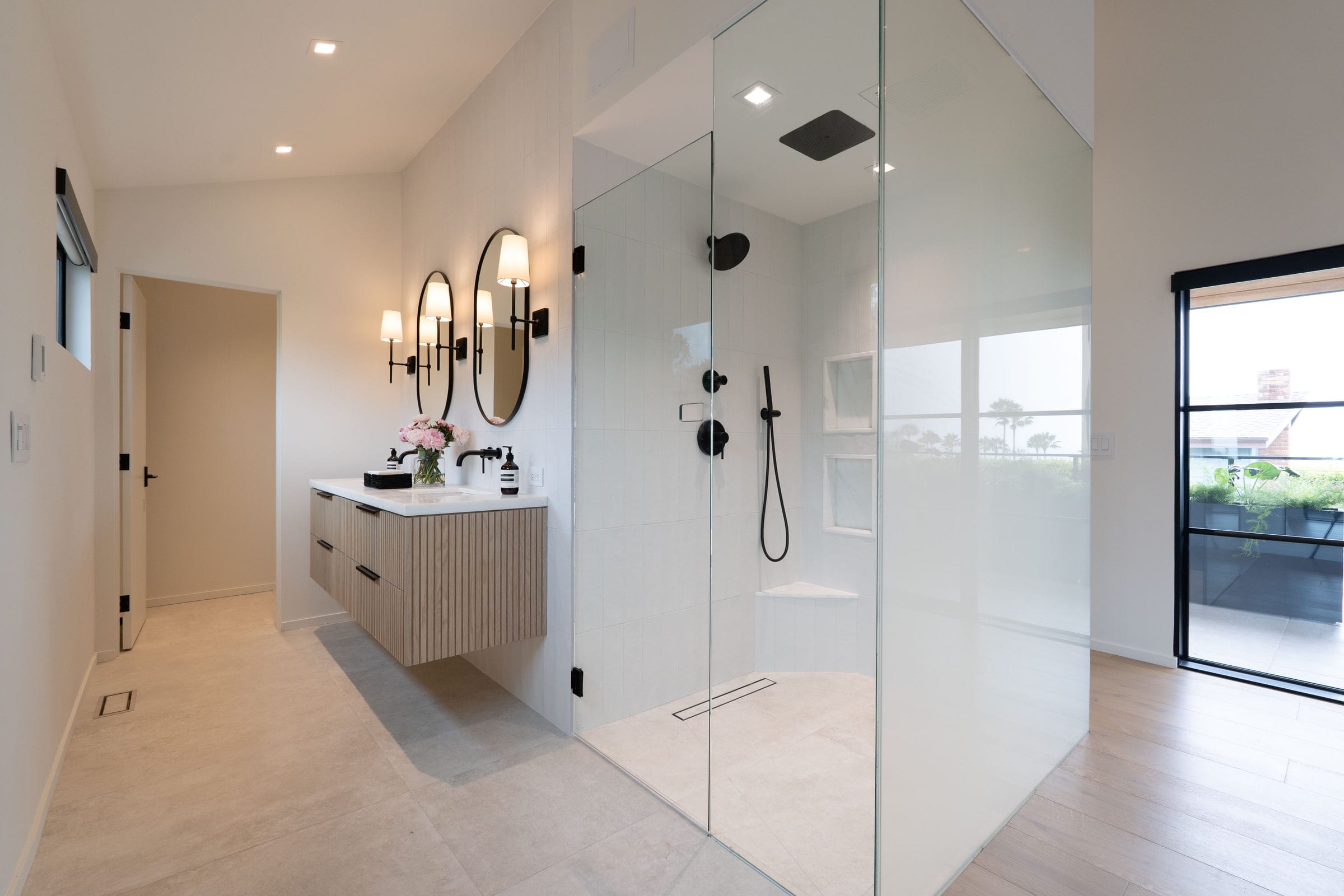 Primary bath with a glass-walled walk-in shower, black fixtures, and an ocean view through the patio doors, DHRH Padaro Lane renovation