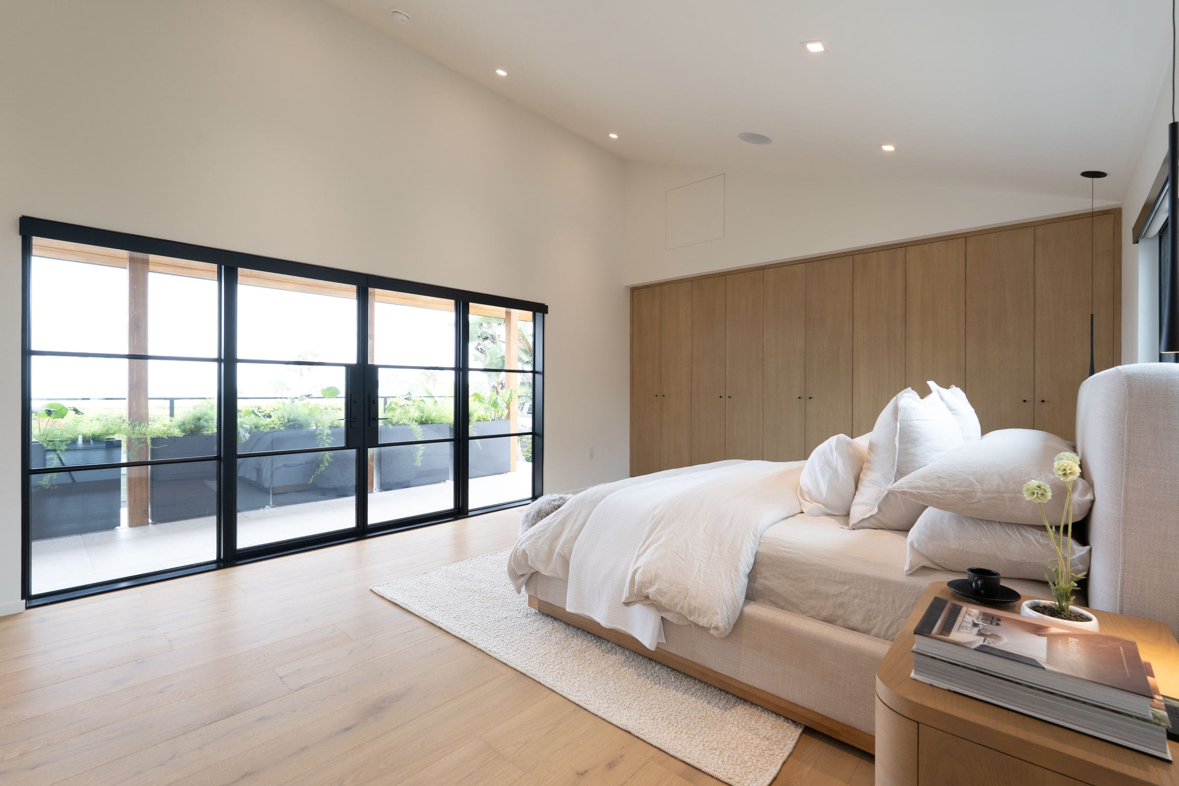 Primary bedroom with floor-to-ceiling steel doors opening to an ocean-view balcony and a built-in oak wardrobe wall, DHRH Padaro Lane renovation
