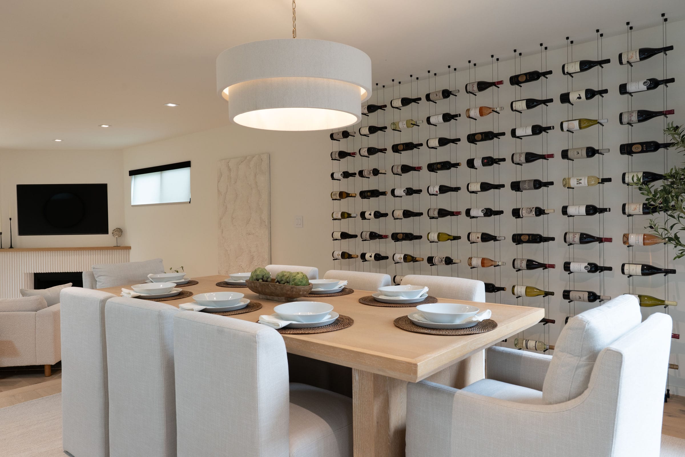 Dining room set for a meal beneath a floor-to-ceiling cable wine wall holding dozens of bottles, DHRH Padaro Lane renovation