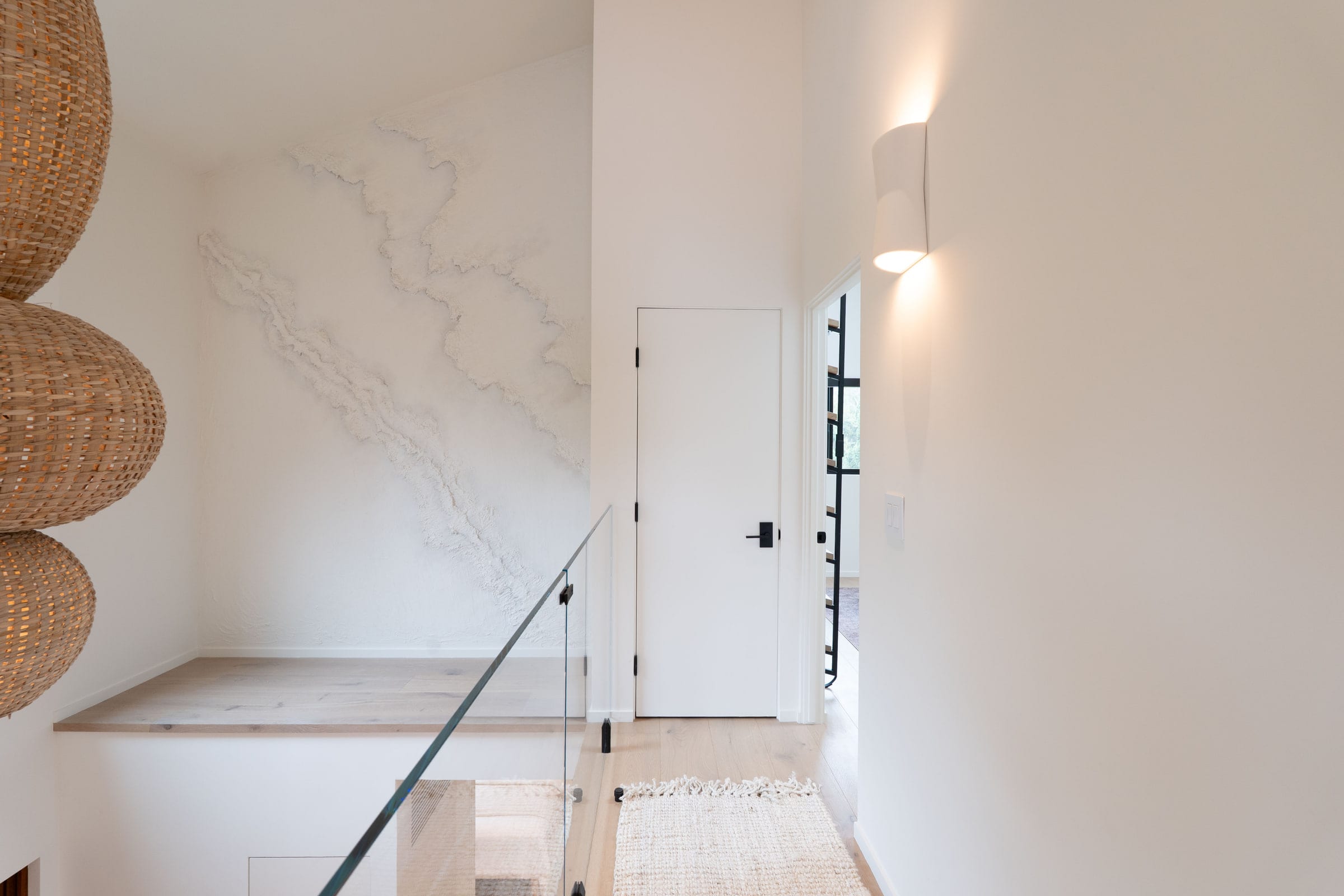 Stairwell landing with a hand-textured plaster accent wall and a three-tier woven rattan pendant light, DHRH Padaro Lane renovation