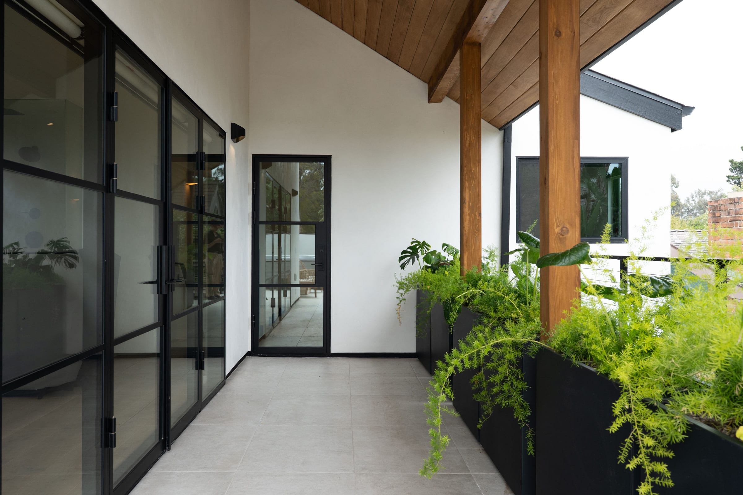 Covered breezeway with black steel-framed glass doors, a wood-beamed ceiling, and potted tropical planters, DHRH Padaro Lane renovation