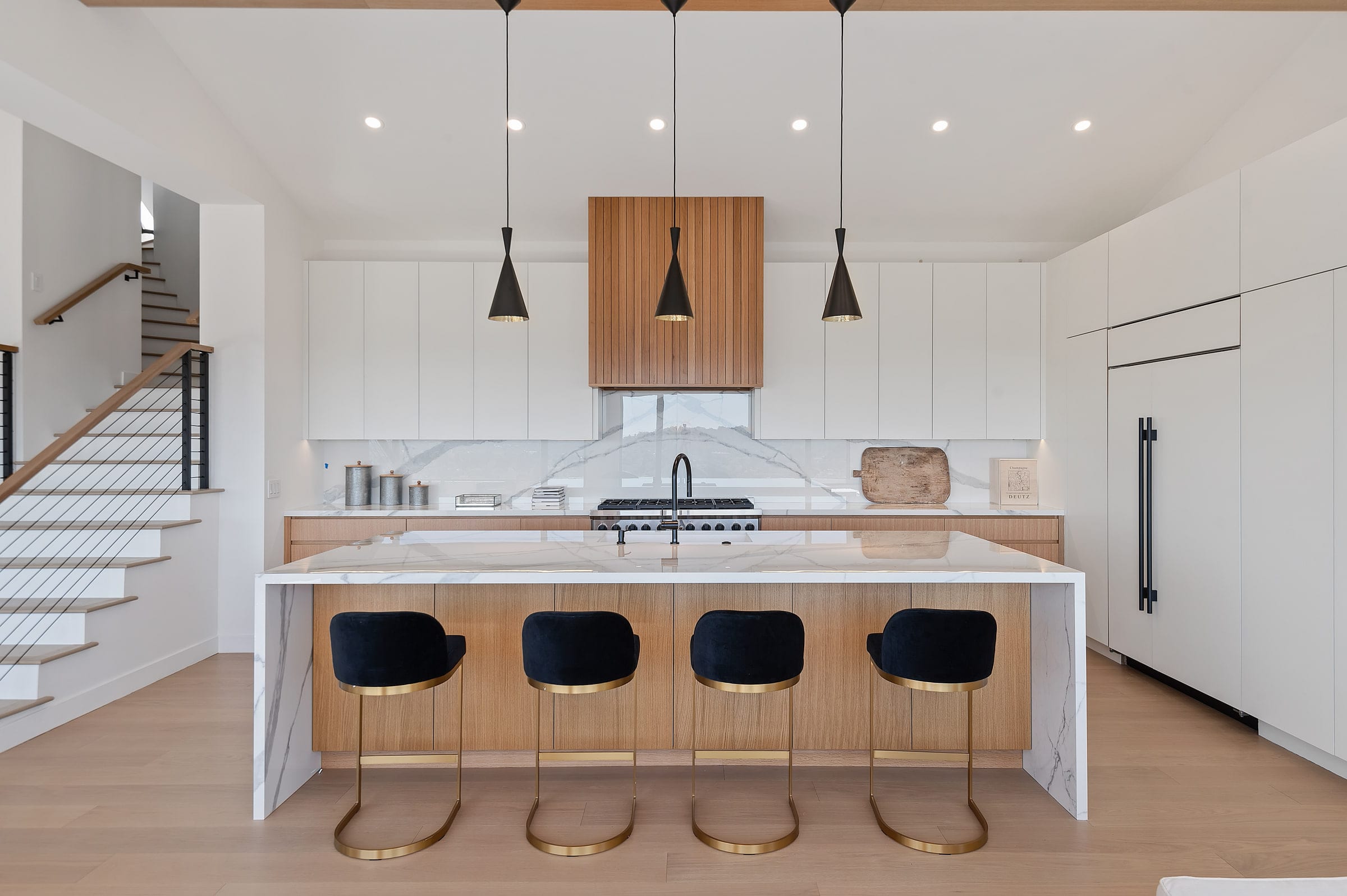 Kitchen island with a marble waterfall counter, black pendant lights, and navy gold-leg barstools, DHRH Riviera renovation