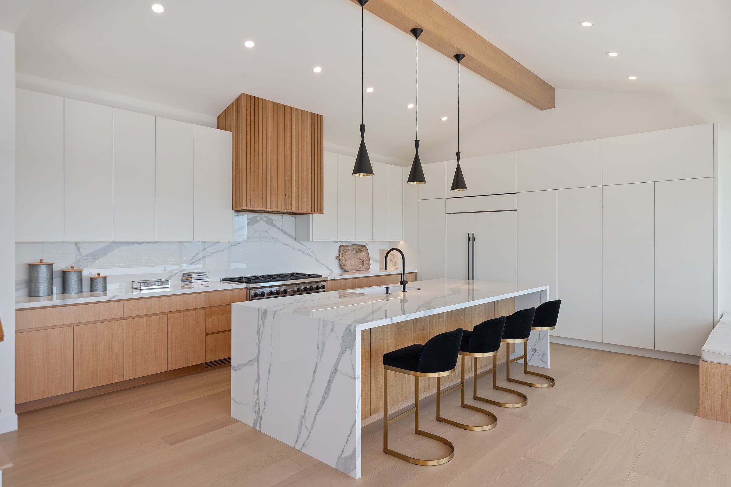 Kitchen island viewed from the staircase, marble waterfall counter and wood-paneled range hood, DHRH Riviera renovation
