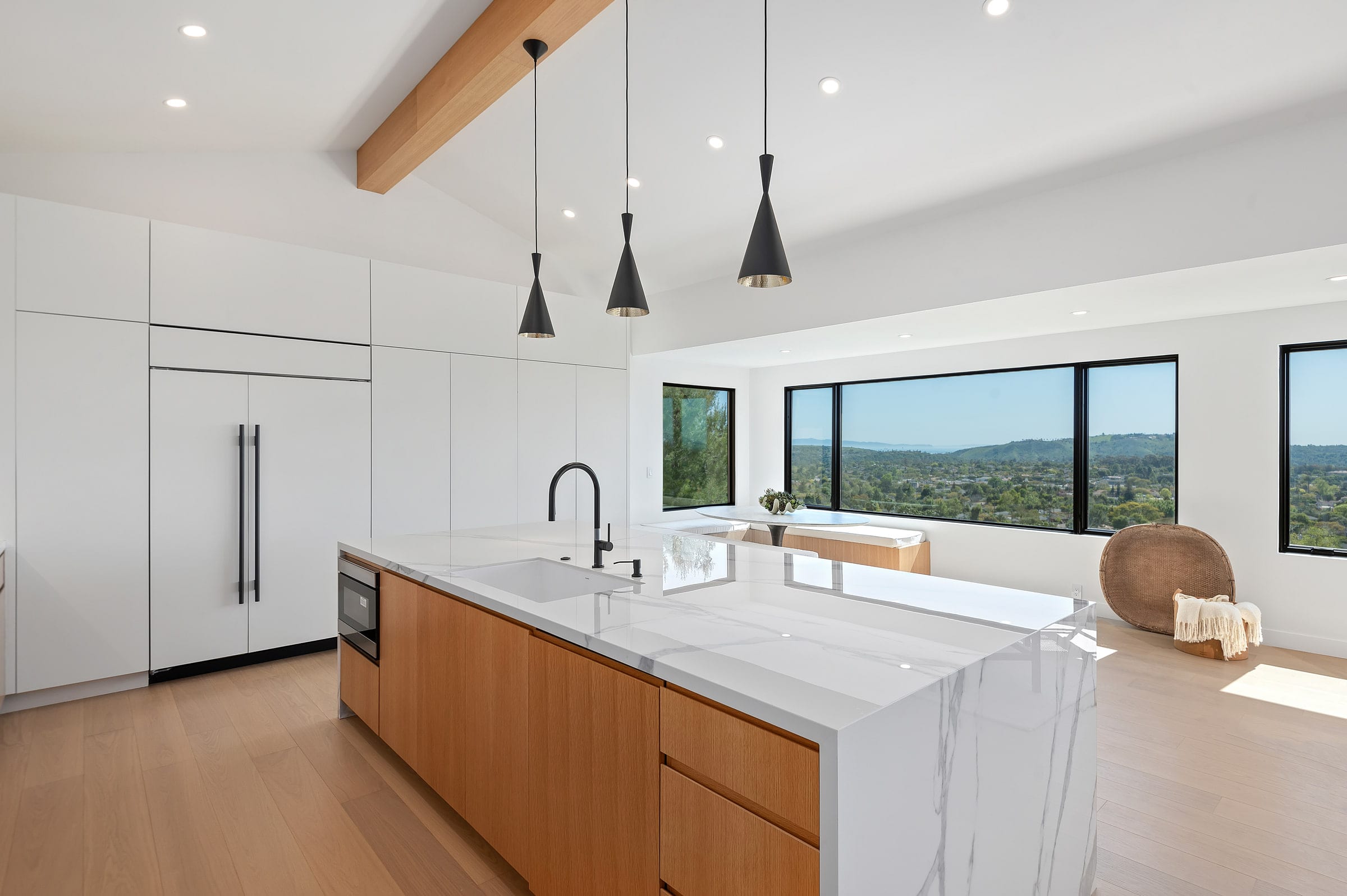 Kitchen island with a marble counter opening to a bay-window dining nook and hillside view, DHRH Riviera renovation