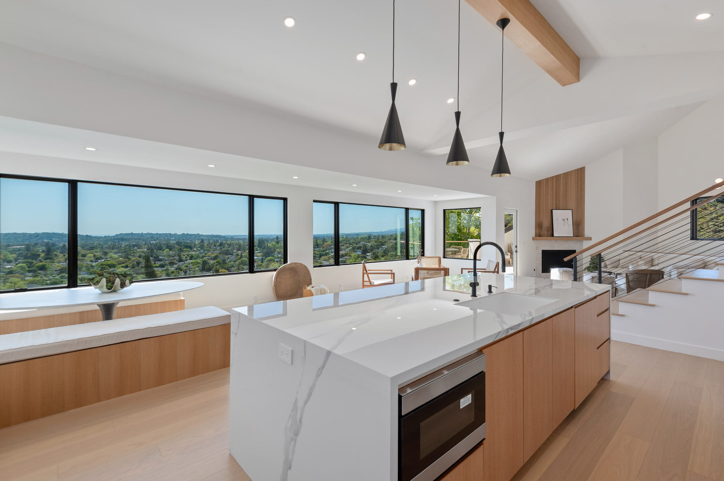 Kitchen island with black pendant lights, an open staircase, and a fireplace beyond the windows, DHRH Riviera renovation