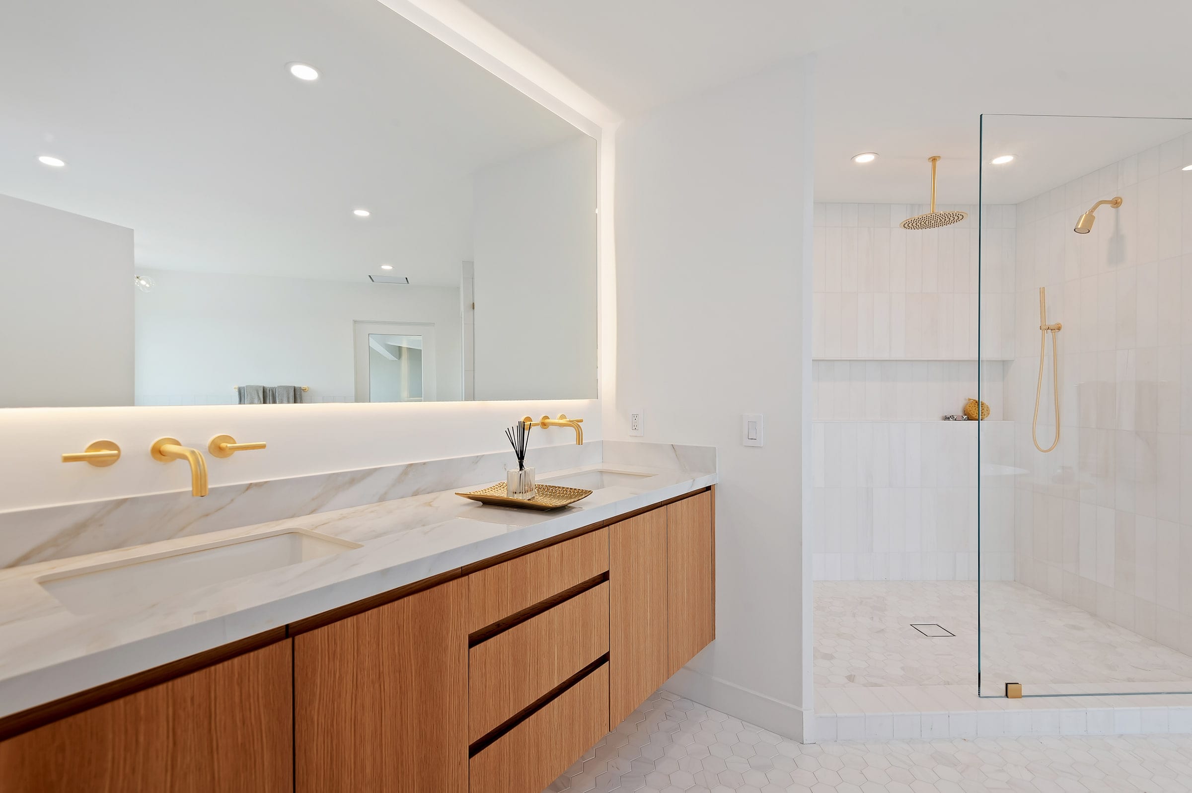 Primary bath double vanity with brass fixtures and marble counters, glass shower beyond, DHRH Riviera renovation