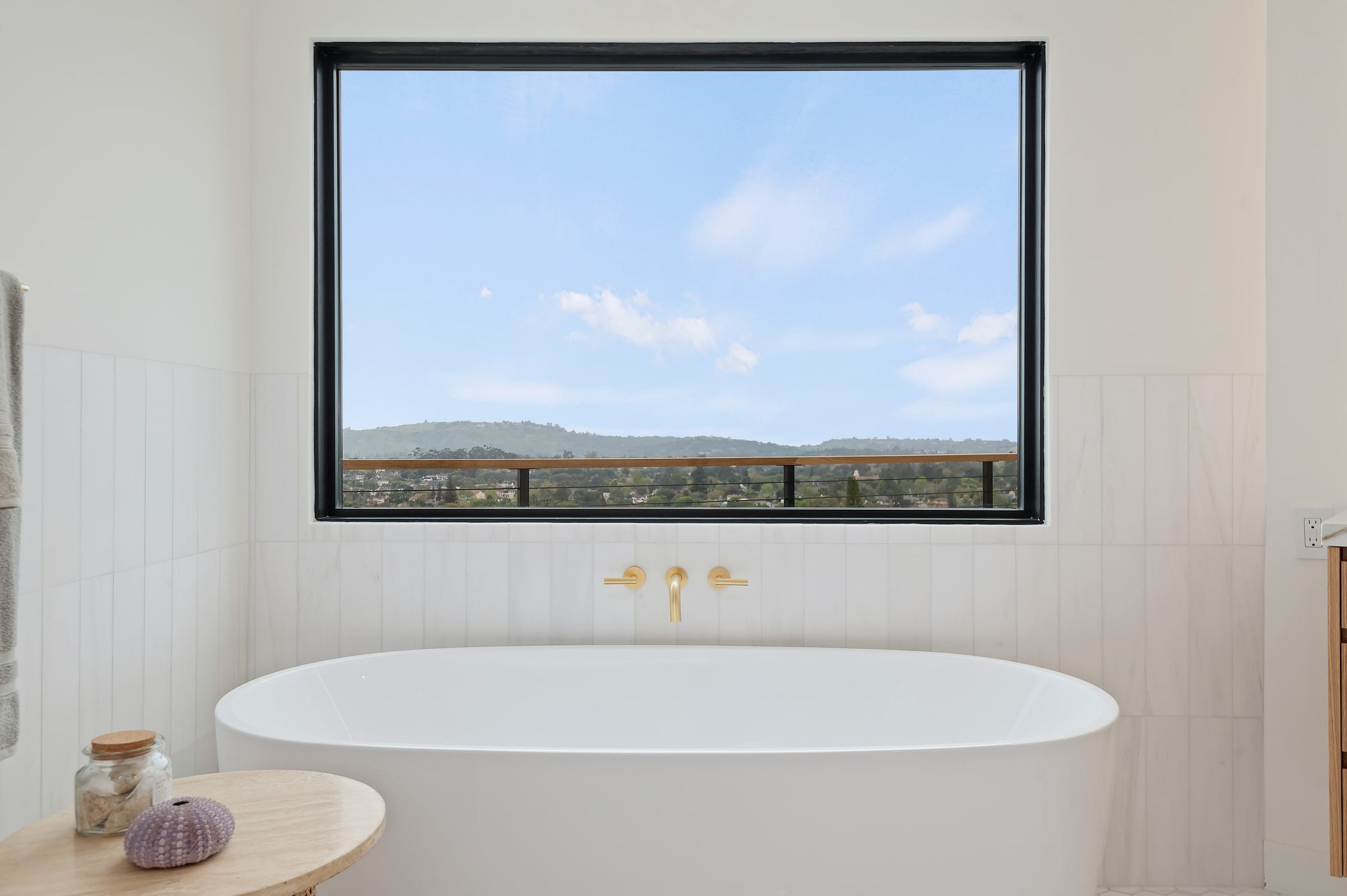 Close-up of the freestanding tub beneath a picture window with a brass tub filler, DHRH Riviera renovation