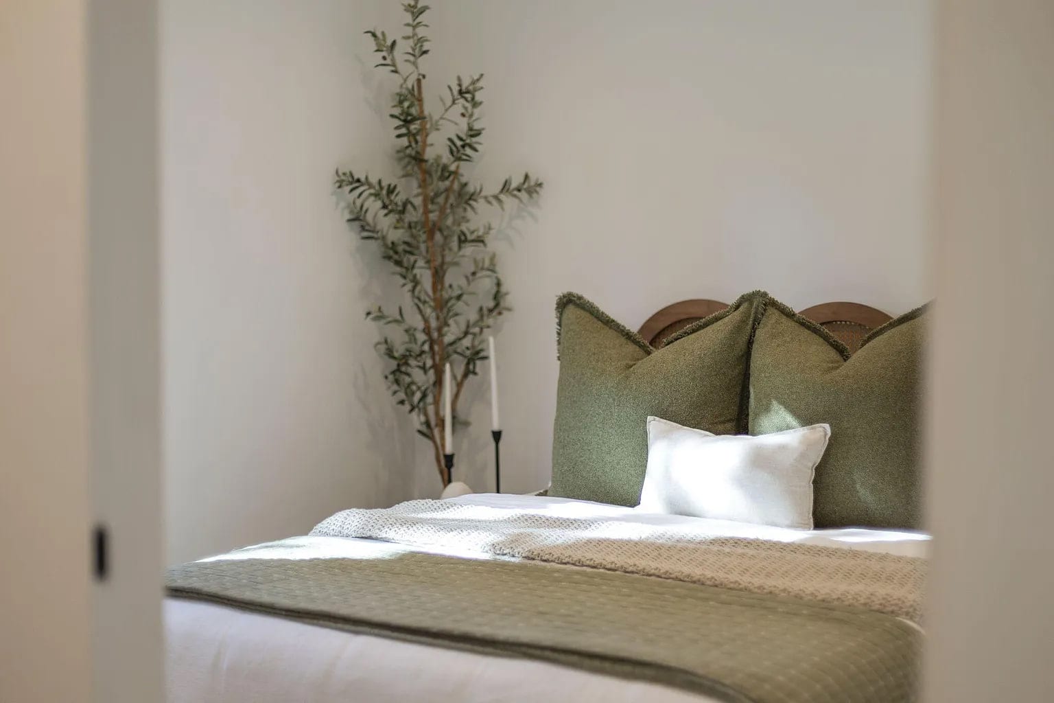 Bedroom doorway view of a cane headboard bed with olive fringed pillows and an olive tree, DHRH San Roque renovation