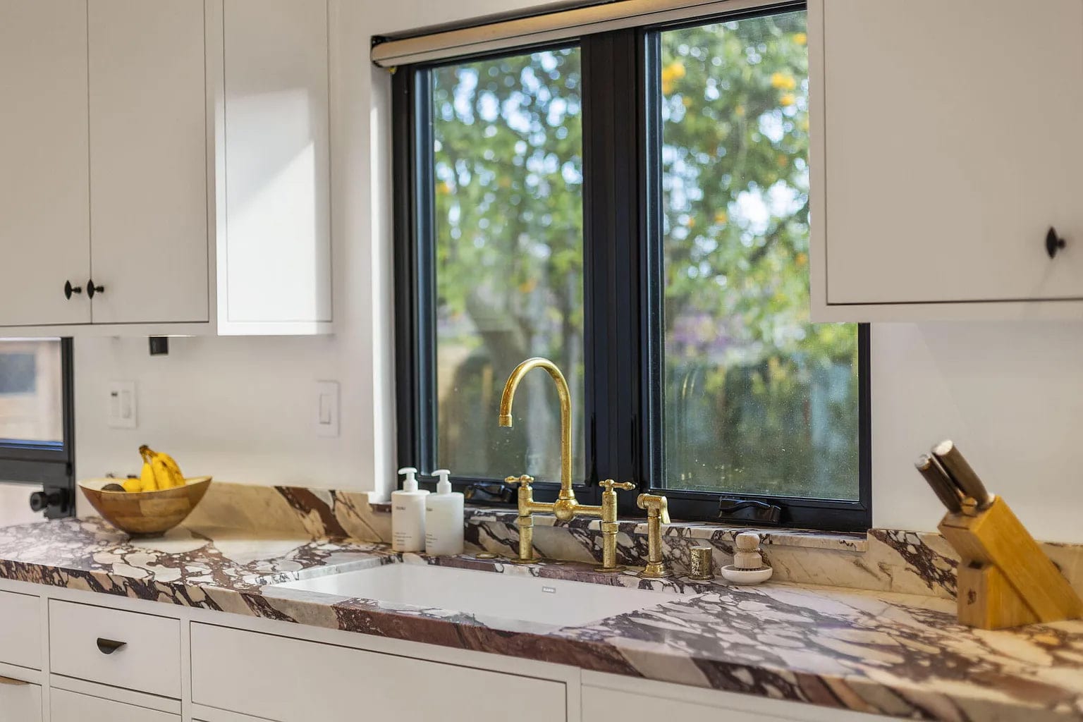 Kitchen sink nook with a brass gooseneck faucet and bookmatched marble backsplash, DHRH San Roque renovation