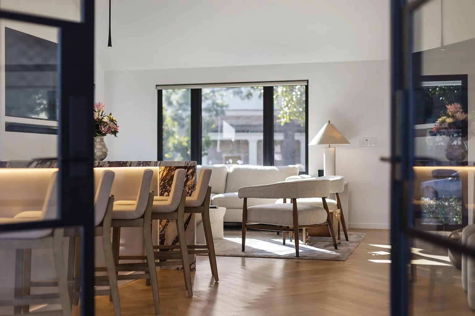 Living room lounge seen through black steel doors, with a marble bar console and boucle chairs, DHRH San Roque renovation