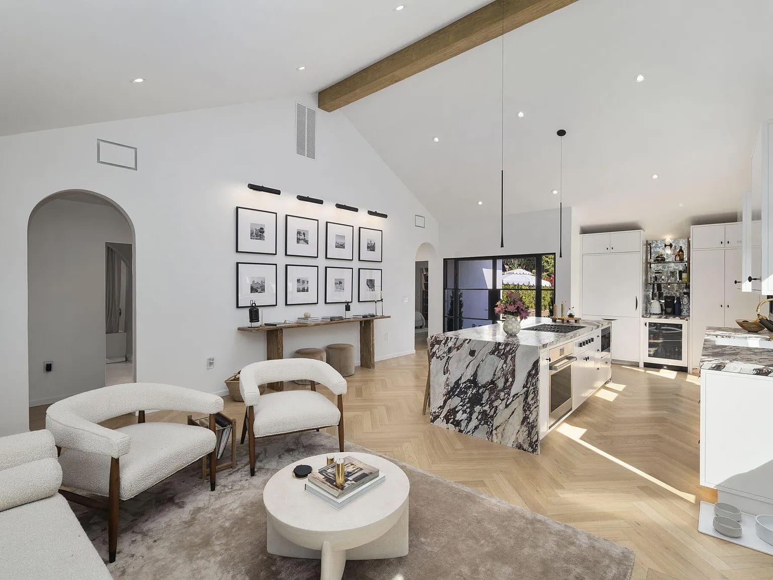 Vaulted living room with a gallery wall, arched doorways, and a marble waterfall island beyond, DHRH San Roque renovation