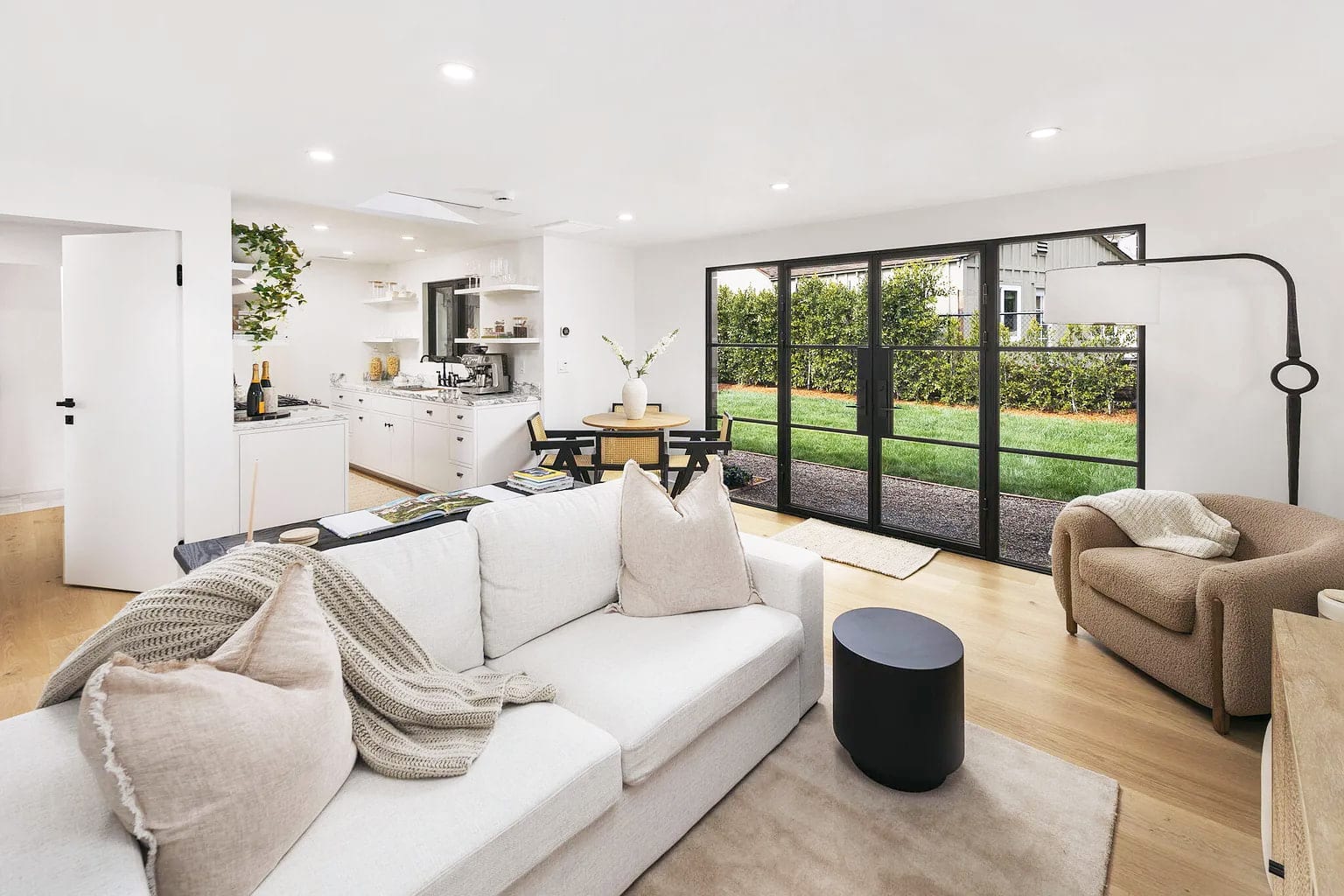 Open living room with a white sectional facing black steel french doors to the backyard, DHRH San Roque renovation