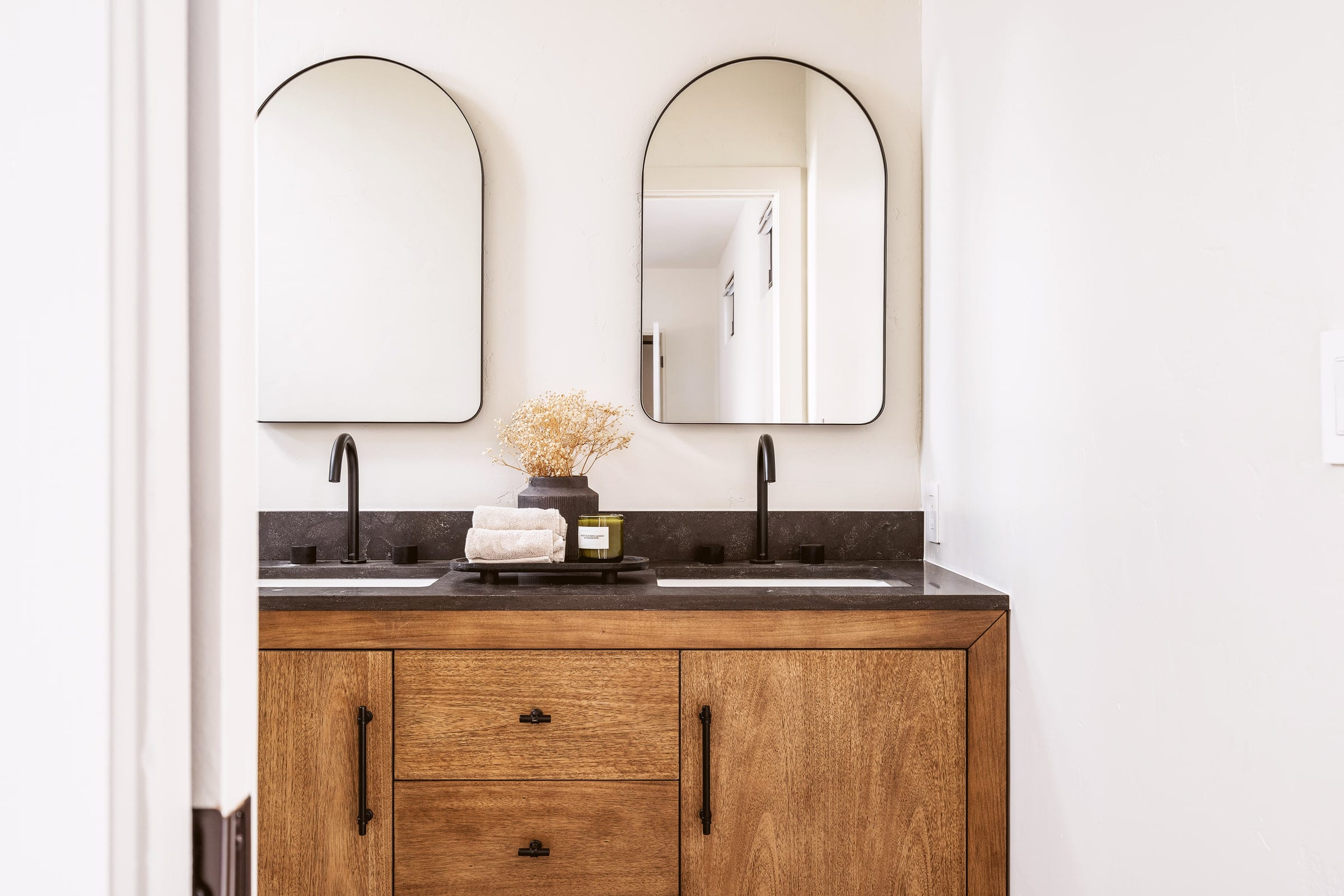 Double vanity bathroom with black stone counters, matte black faucets, and twin arched black-framed mirrors, DHRH West Side renovation