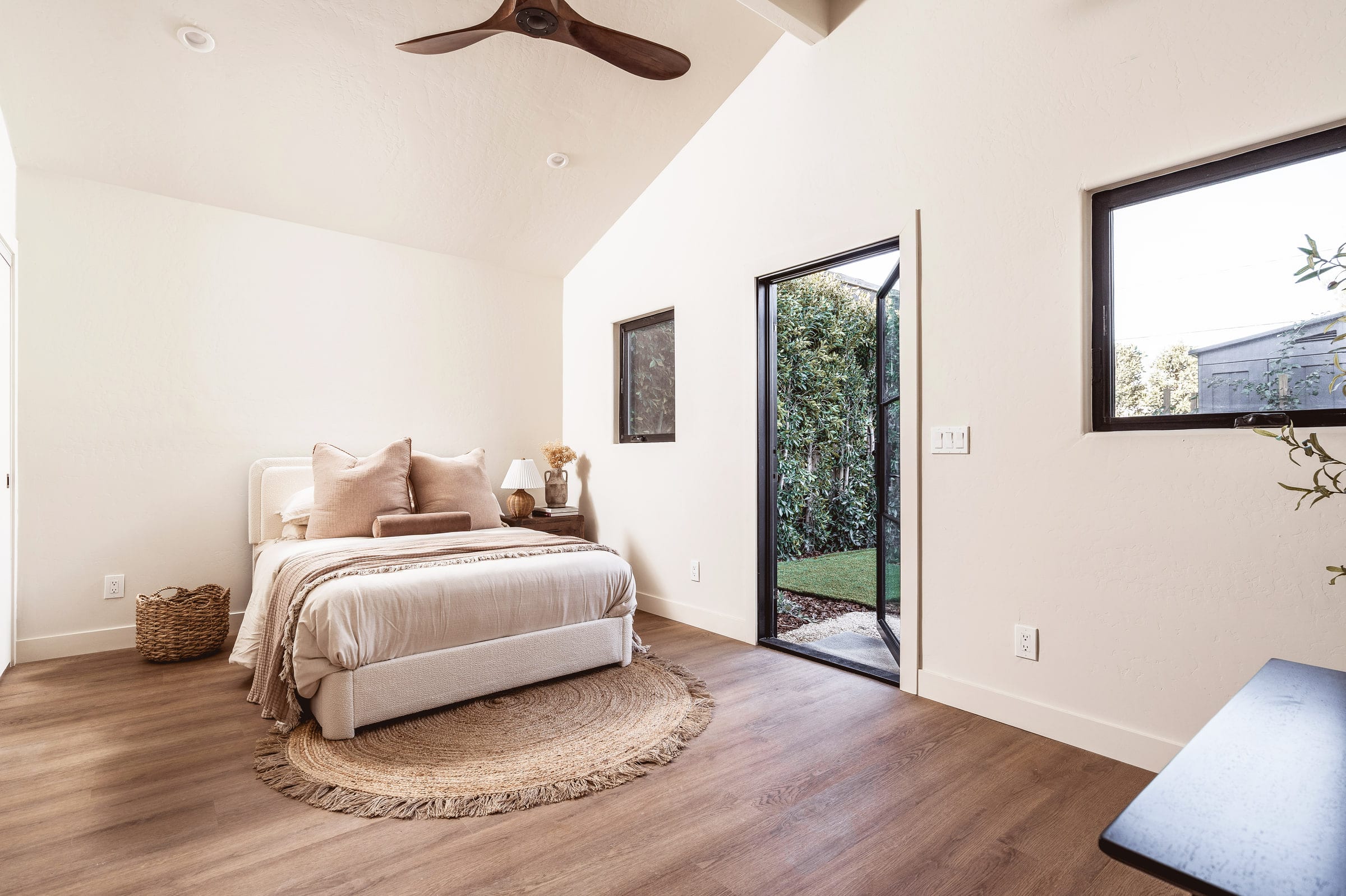 Vaulted bedroom with a wood ceiling fan, upholstered bed, jute rug, and a steel-framed door to the garden, DHRH West Side renovation