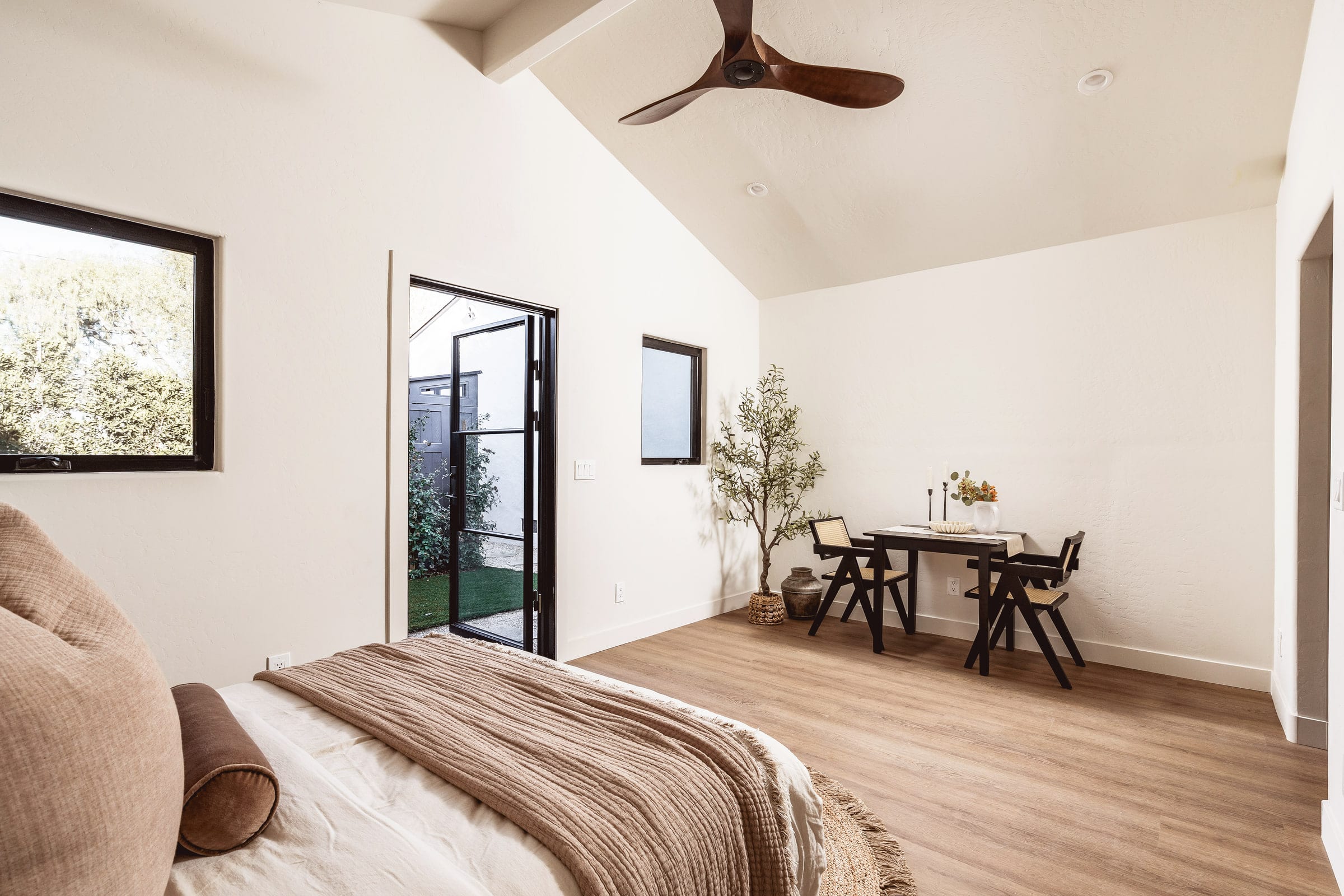 Bedroom sitting nook with a small dining table, woven chairs, and an olive tree beside the garden door, DHRH West Side renovation