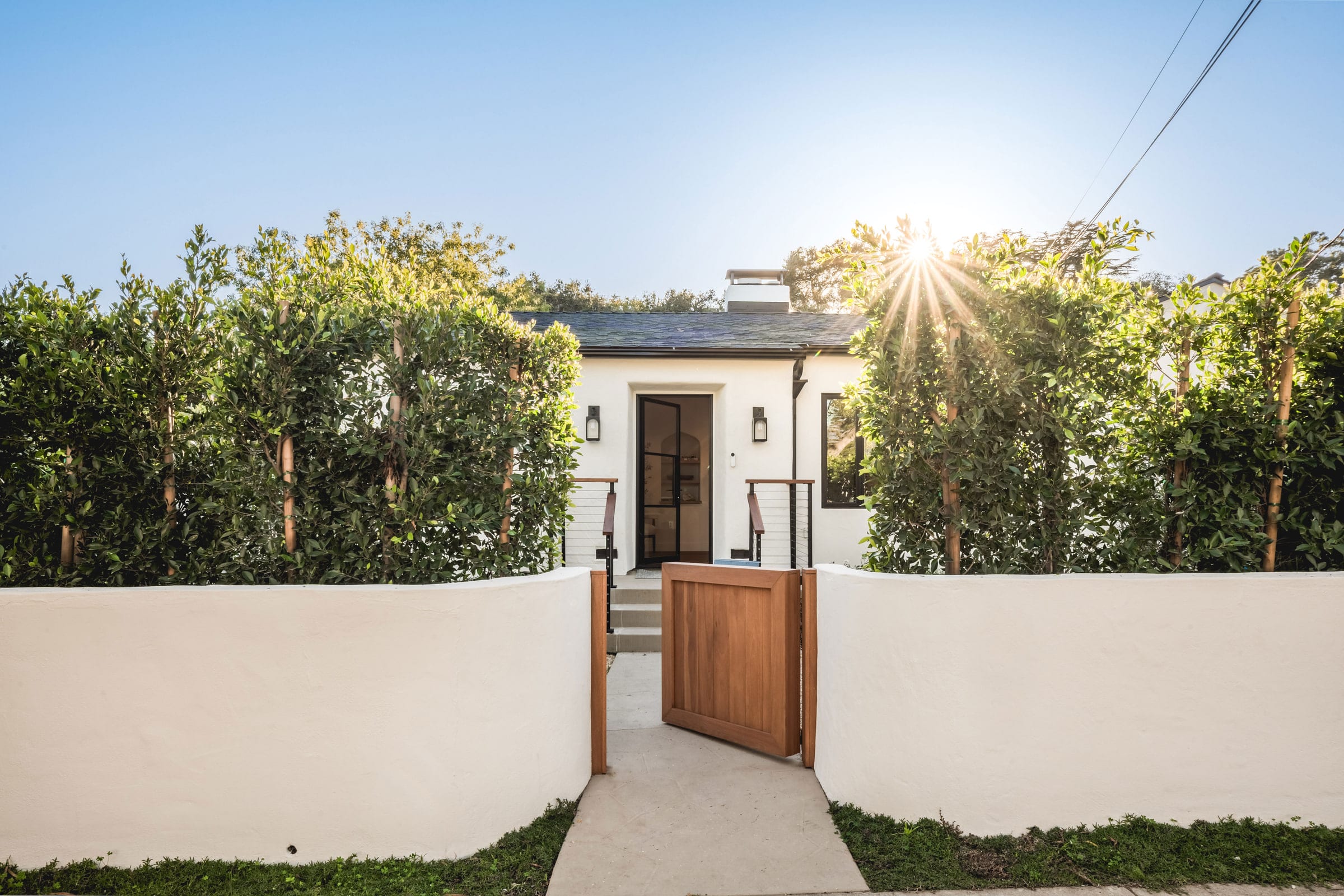 White stucco garden wall and wood gate framed by hedges leading to the cottage's front entry, DHRH West Side renovation