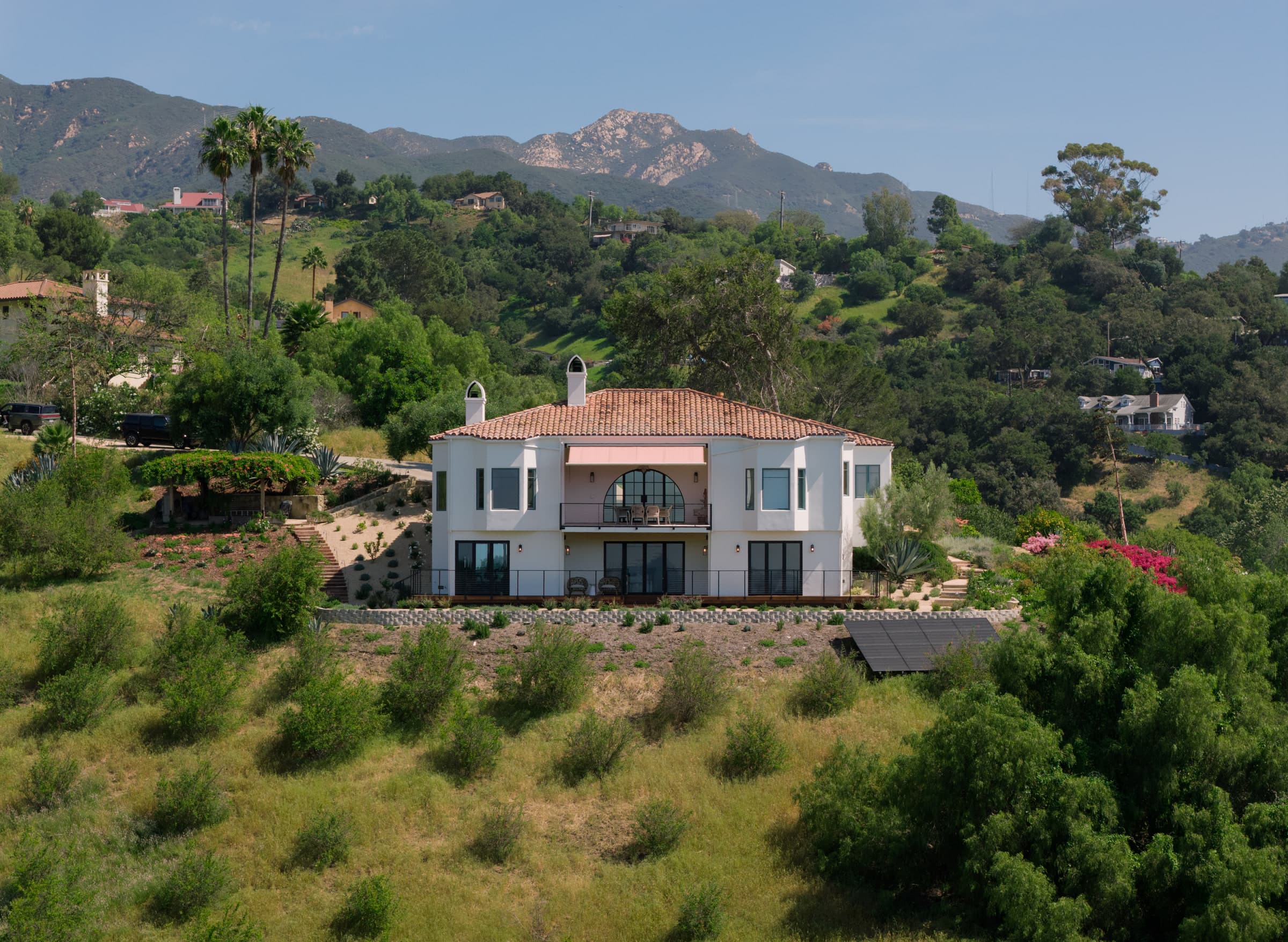 Hillside Spanish-style villa with a red clay tile roof and white stucco exterior among oaks and palms, DHRH Mission Canyon renovation