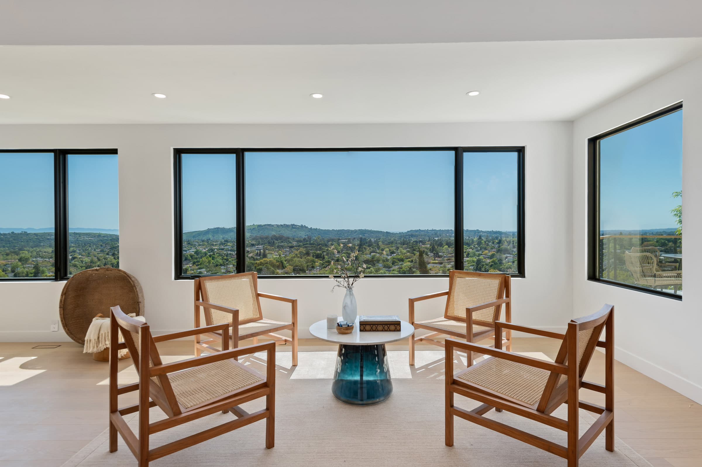 Living room seating with cane lounge chairs around a blue glass coffee table and hillside-view windows, DHRH Riviera renovation